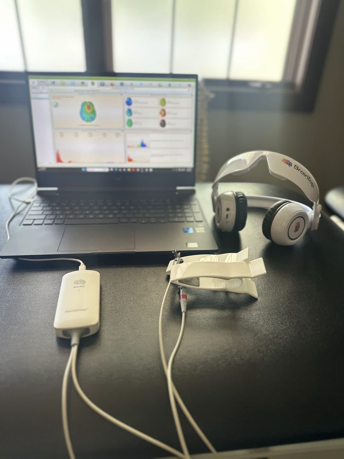 NeuralChek scan setup in Dr. Maxa's office — laptop with results, BrainTap headset, and sensors